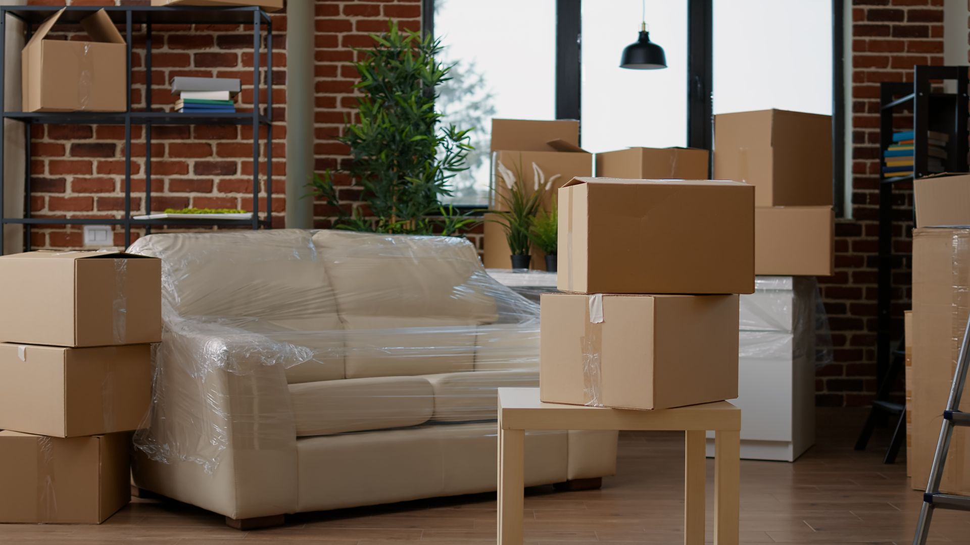 Interior view with moving boxes and furniture wrapped in plastic, indicating a move.