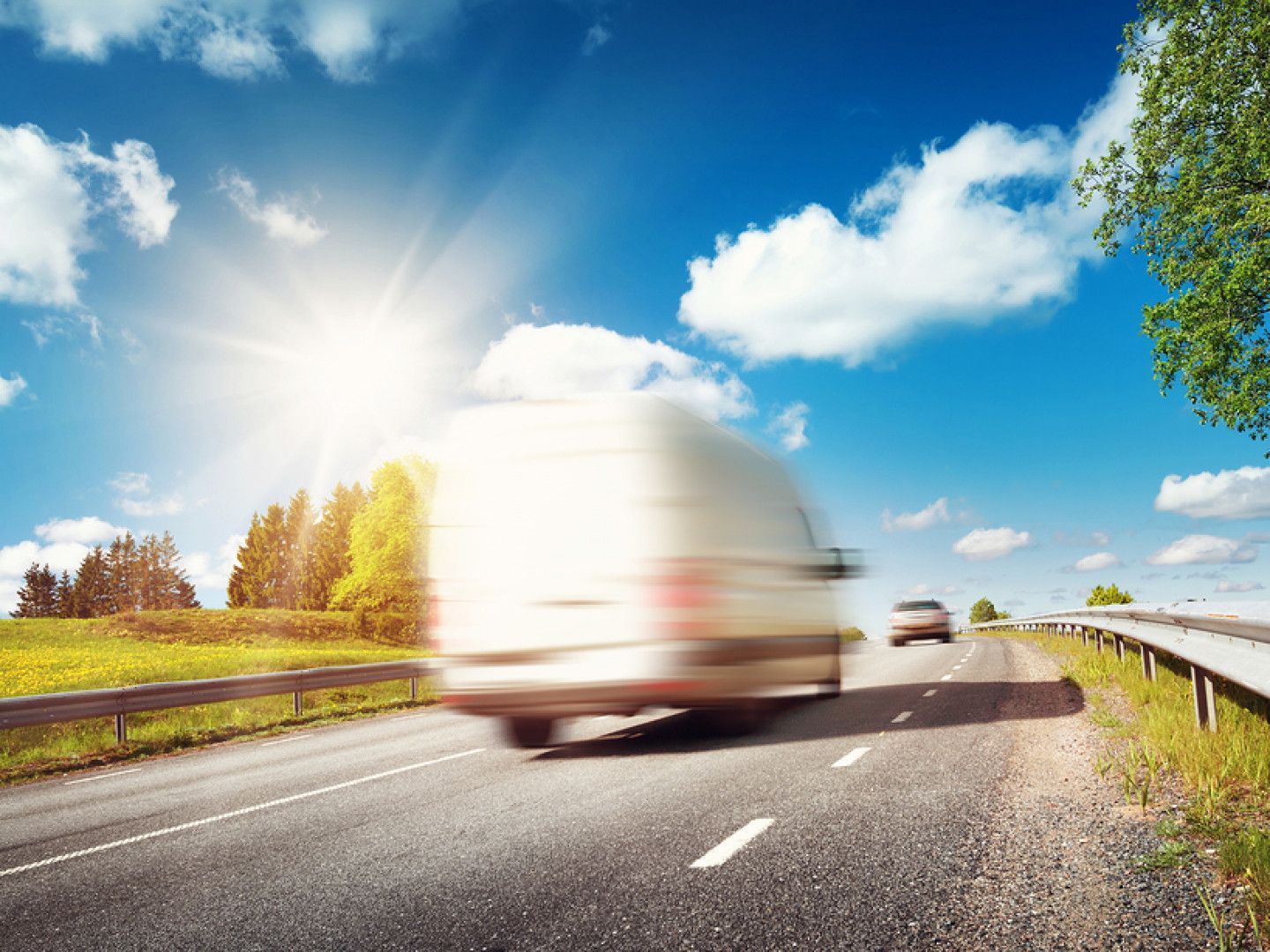 White delivery van speeding down a sunny highway with blurred motion.
