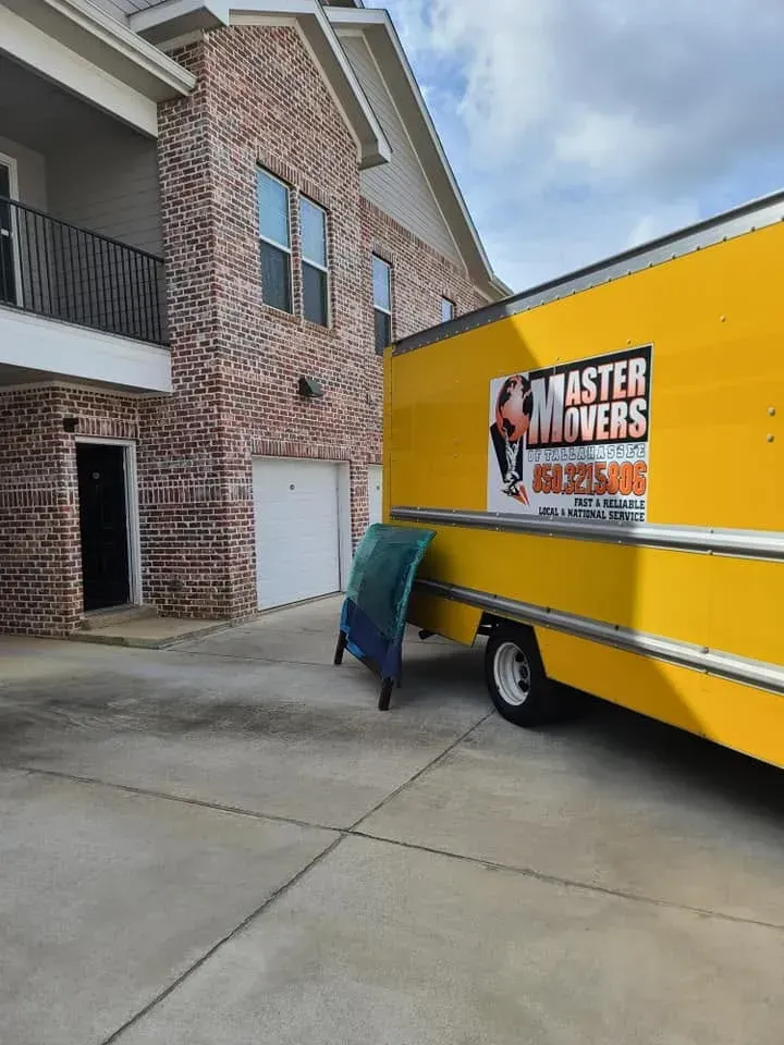 Master Movers of Tallahassee truck parked outside a brick apartment building with a folded mattress