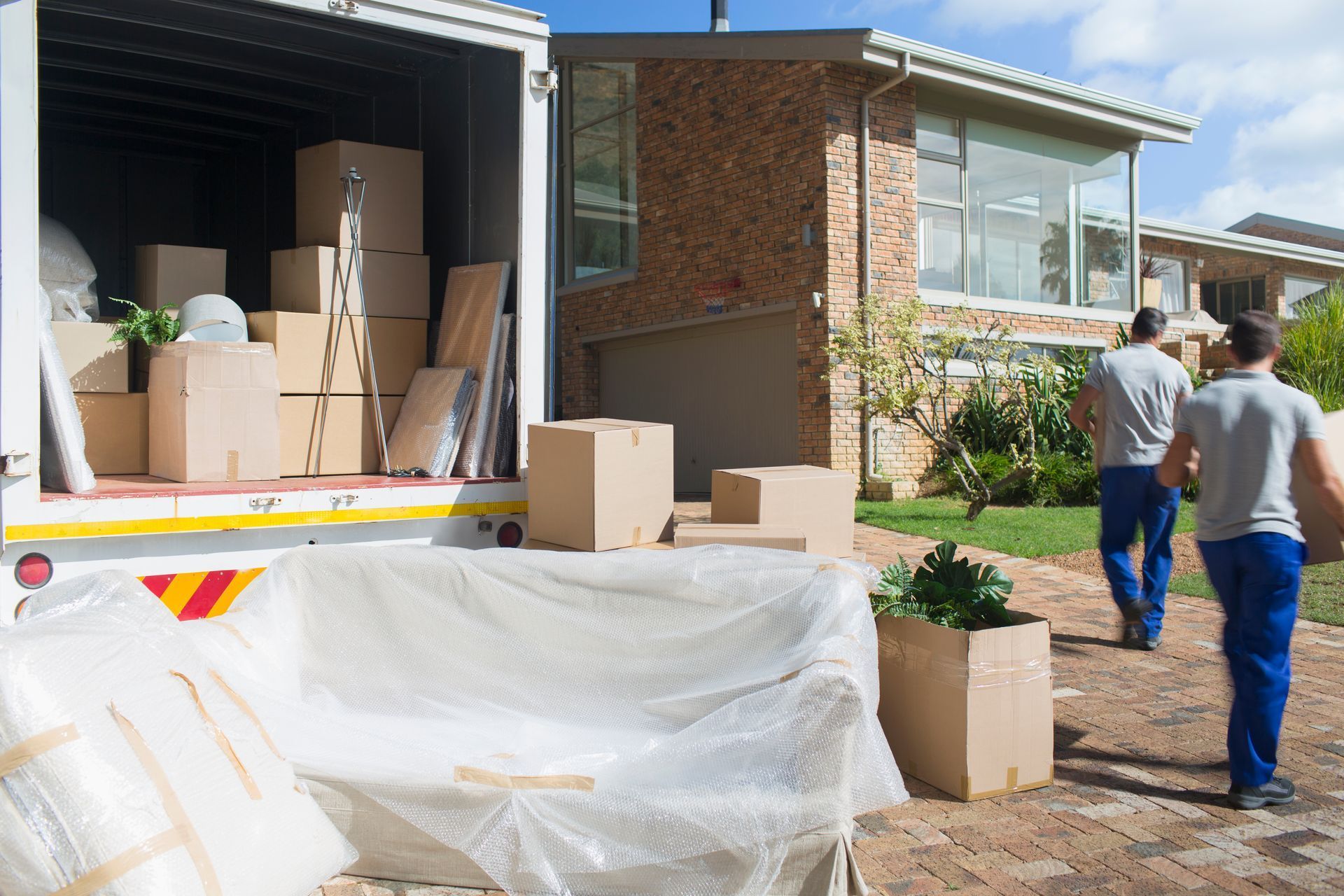 Two movers carrying boxes from a house into a moving truck.